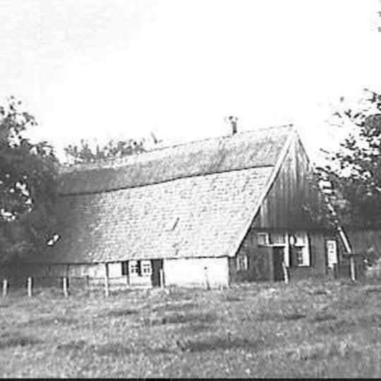 Boerderij, grotendeels in vakwerk, met houten topgevels, die iets overkraagd zijn. Achterbaander in underschoer
