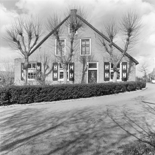 Boerderij met woongedeelte onder rieten zadeldak en hogere schuur, eveneens onder met riet gedekt zadeldak. In de puntgevel van het woonhuis vensters met luiken en zesruitsschuiframen.