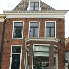 Hoekpand onder diep zadeldak tegen achtertopgevel en voorgevel met rechte kroonlijst, dakkapel en schoorsteen