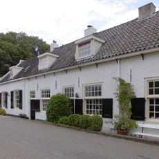 Gepleisterd laag huis, ramen met kleine roeden en halve luiken, zadeldak