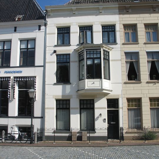 Linkerdeel van pand met gepleisterde lijstgevel onder dwars schilddak en erker op de verdieping