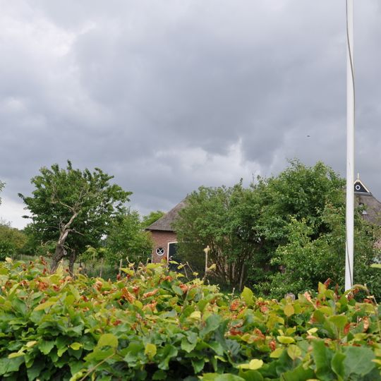 Boerderij uit de eerste helft der 19e eeuw onder hoog wolfdak, dat deels met pannen, deels met riet en deels met golfijzer is gedekt