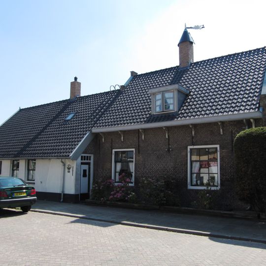 Huis, tegen de dijk gebouwd, gedateerd in de zuidgevel onder pannen zadeldak, waarop een schoorsteen met gesneden gek. Vensters met negenruitsramen en luiken