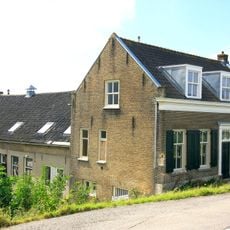 Gaaf bewaard dwarshuis, onder zadeldak met dakkapel. Dubbele deur in omlijsting door pilasters met hoofdgestel. Vensters met luiken en zesruitsschuiframen