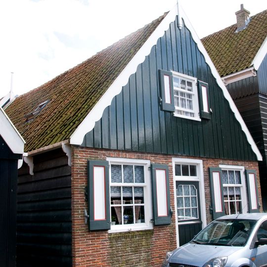 Houten huis met daklijsten op consoles en een vernieuwde voorgevel met bakstenen pui