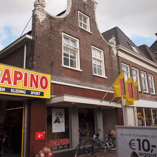 Pand onder zadeldak tegen klokgevel met gebeeldhouwde lijsten en aanzetkrullen en beeldhouwwerk in de top