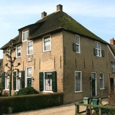 Pand met verdieping onder rieten schilddak. Tweelichtkozijn met luiken. Vormt een geheel met de buurnummers 12-13