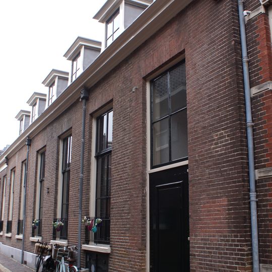 Verdiepingsloos, plat afgedekt pand, opgetrokken in baksteen met natuurstenen sokkel, voorzien van een drietal zesruits schuifvensters en een kroonlijst