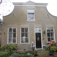 Dorpshuis onder zadeldak tussen ingezwenkte afgeknotte halsgevel en puntgevel achter