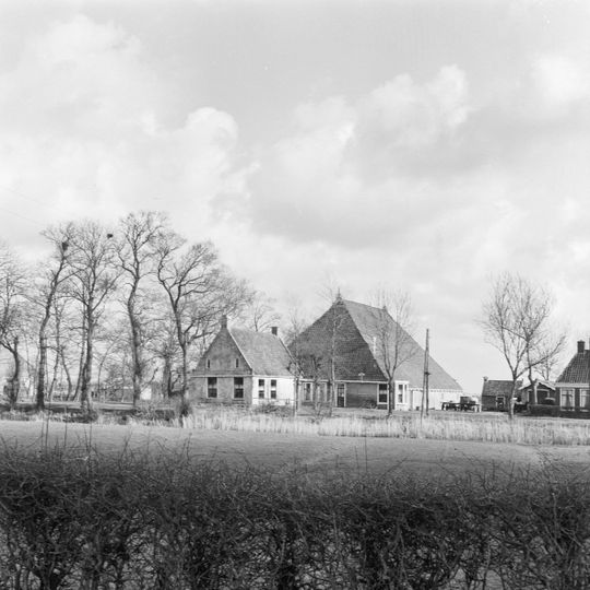 Grote kop-rompboerderij met alleen achteraan onderkelderd voorhuis, gepleisterde topgevel met gesloten top met kleine lichtopeningen en omlopende houten goot