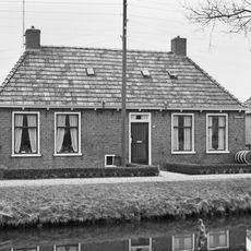 Dubbel landelijk pand met goot op klossen onder schilddak met twee hoekschoorstenen (vormt een geheel met nr. 24)