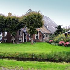 Kop-rompboerderij met onderkelderd voorhuis en houten beschieting met sierlijst boven de inrit van de schuur