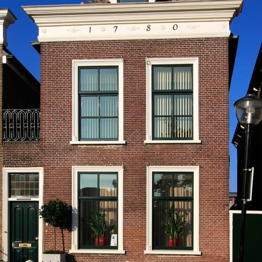 Pand met lijstgevel twee vensterassen breed. Geprofileerde houten vensteromlijstingen. Gietijzeren stoephek met hardstenen palen. Ouder pand met schilddak