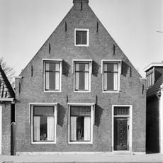 Woonhuis onder zadeldak tegen forse topgevel met beitelingen langs de zijden