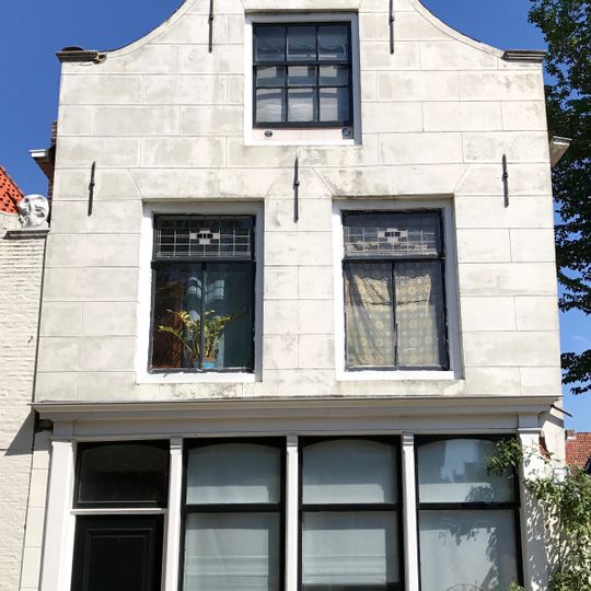 Hoger pand onder zadeldak tegen gepleisterde, ingezwenkte en door driezijdig fronton bekroonde halsgevel