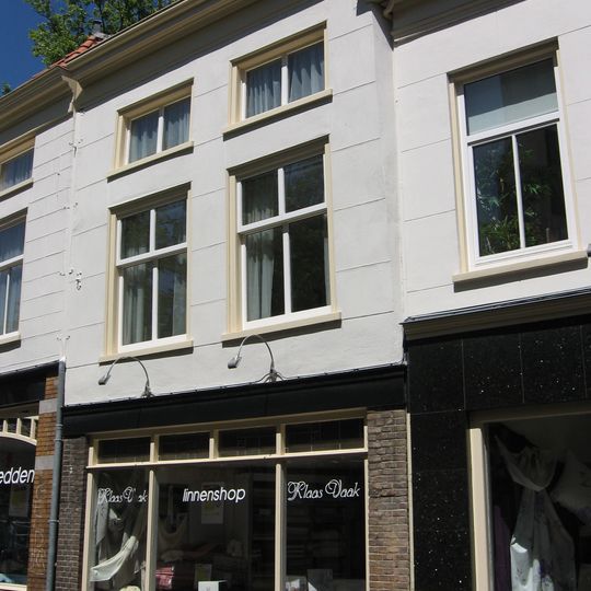 Gerend pand onder schilddak. Gepleisterde lijstgevel met lage bovenverdieping. In de verdieping zesruitsschuiframen