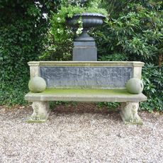 Twickel: gietijzeren tuinvaas achter de tuinbank in de oranjerietuin (donkergrijs geschilderd) in schaalvorm op sokkel van beton