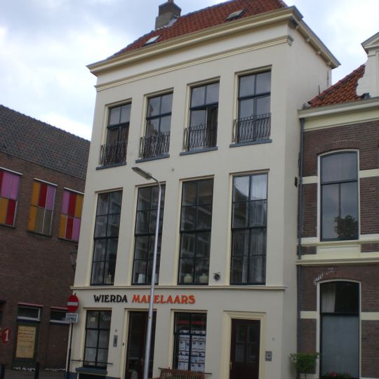 Huis met gepleisterde lijstgevel, aan voorzijde met verdieping onder schilddak met hoekschoorstenen verhoogd