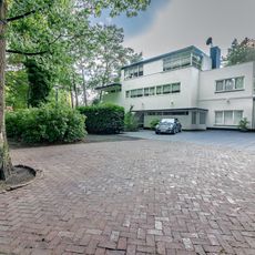 Vrijstaand, in baksteen opgetrokken, witgepleisterd, vlakgedekt woonhuis met verdieping