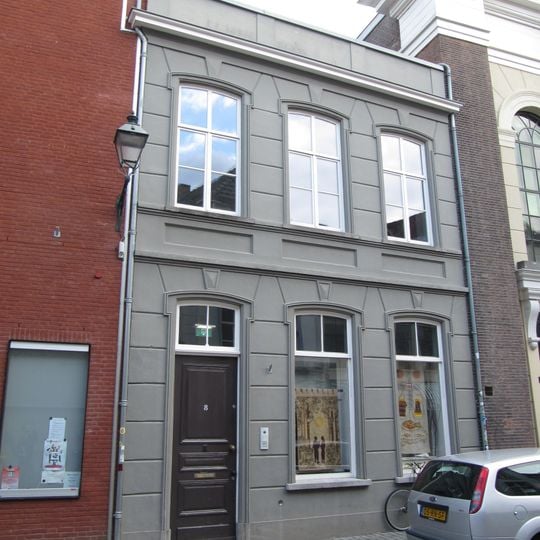 Huis met gebosseerd gepleisterde lijstgevel, bekroond door een attiek en voorzien van segmentvormig overtoogde vensters