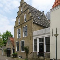 Ondiep pand onder zadeldak tussen topgevel achter en trapvormige voorgevel