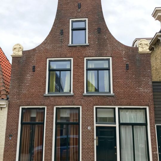 Pand onder zadeldak tegen vernieuwde halsgevel met gebeeldhouwde aanzetkrullen en natuurstenen deklijst