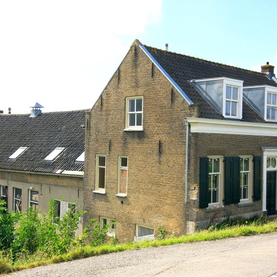 Gaaf bewaard dwarshuis, onder zadeldak met dakkapel. Dubbele deur in omlijsting door pilasters met hoofdgestel. Vensters met luiken en zesruitsschuiframen