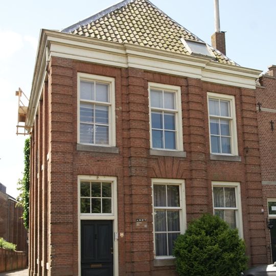 Huis onder schilddak en met lijstgevel, ingedeeld door een middenrisaliet en bakstenen geblokte pilasters