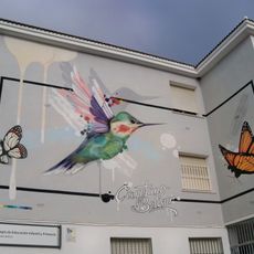 Mural con el nombre del colegio Cayetano Bolívar junto a la imagen de un colibrí y dos mariposas.