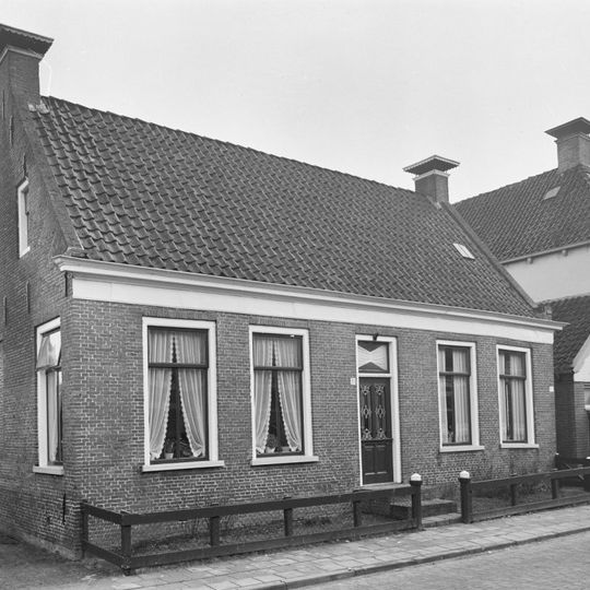 Eenvoudig dorpshuis onder zadeldak tussen zijtopgevels met schoorstenen waarop borden