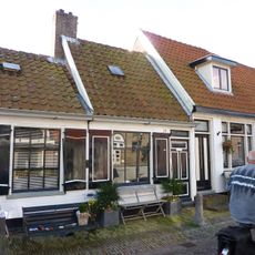 Klein huisje onder een dwars dak met de nummers 10 en 12. Aardige details aan vensters, luiken en achterschot