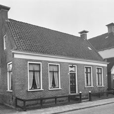 Eenvoudig dorpshuis onder zadeldak tussen zijtopgevels met schoorstenen waarop borden