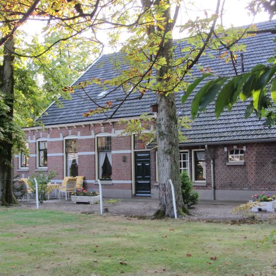 De Mans: boerderij van het hallehuistype opgetrokken in bruine baksteen onder een met zwarte muldenpannen gedekt zadeldak dat boven het uitgebouwde woonhuisgedeelte is geknikt