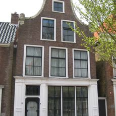 Hoog pand onder zadeldak tegen klokgevel met gebeeldhouwde aanzetkrullen, deklijst en kuifstuk