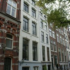 Pand met smalle met gepleisterde gevel onder rechte lijst en voorzien van vensteromlijstingen