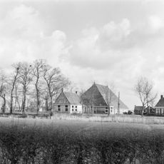 Grote kop-rompboerderij met alleen achteraan onderkelderd voorhuis, gepleisterde topgevel met gesloten top met kleine lichtopeningen en omlopende houten goot