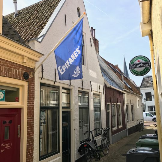 Pand onder zadeldak tegen puntgevel met beitelingen en rond topvenster