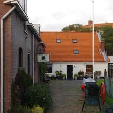 Ten dele gepleisterd molenaarshuis onder een met pannen gedekt zadeldak tussen puntgevels met vlechtingen