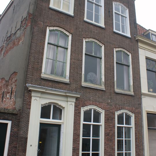Pand met hoge bakstenen gevel, pilasters in bovenverdieping nauwelijks zichtbaar, rechte kroonlijst
