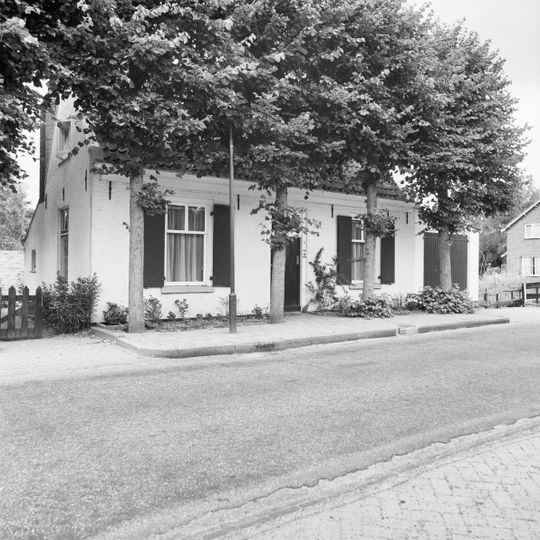 Gepleisterd dwarshuis onder pannen zadeldak tussen puntgevels. Vensters met luiken in de voorgevel