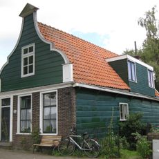 Houten dijkhuis met klokgevel (uit- en ingezwenkt voorschot) uit de 19de eeuw, bakstenen onderpui in empire stijl