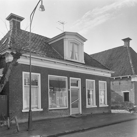 Eenvoudig pand met geblokte kroonlijst onder schilddak met hoekschoorstenen waarop borden